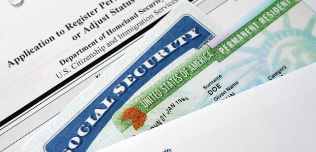 Close-up of a U.S. Social Security card partially overlapping a U.S. Permanent Resident card, also known as a green card. Both cards are resting on top of an Application to Register Permanent Residence or Adjust Status form from the U.S. Citizenship and Immigration Services, often handled by Lancaster Immigration Lawyers.