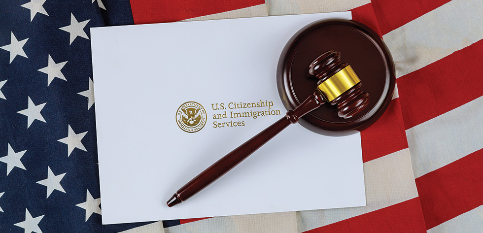 A wooden gavel rests atop an envelope from the U.S. Citizenship and Immigration Services, symbolizing the guidance offered by Lancaster Immigration Lawyers. The background is composed of overlapping American flags.